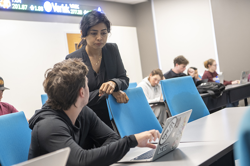 a professor looks over a student's shoulder as they discuss something on his laptop