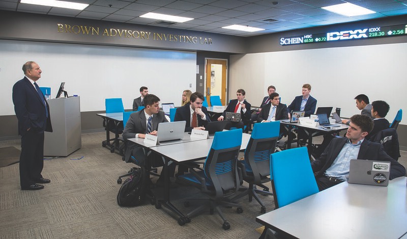 Eleven formally-dressed students work in the Brown Advisory Investing Lab under the supervision of an older advisor.