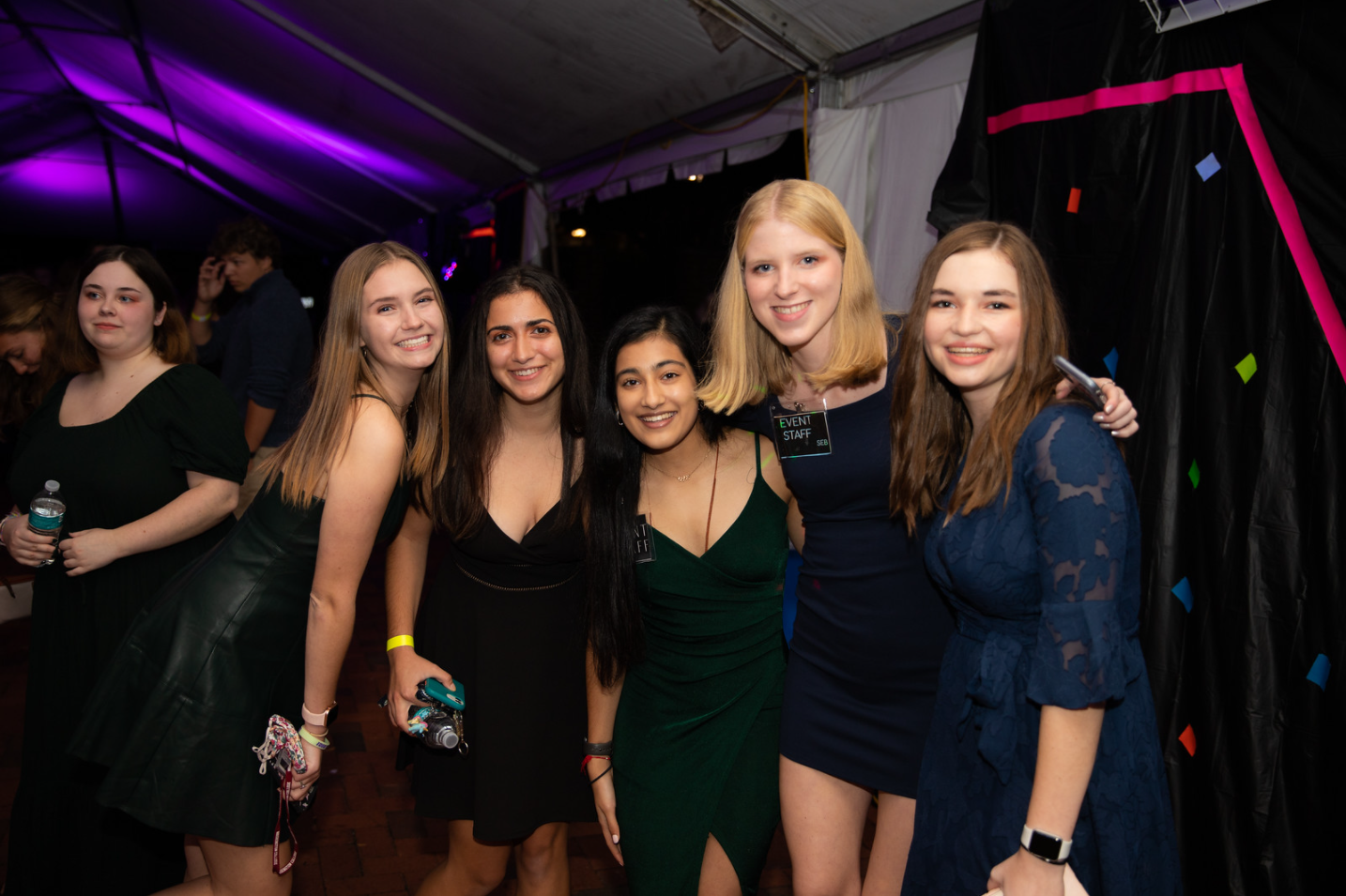 Four people in formal wear pose and smile for the camera with party decorations behind them.