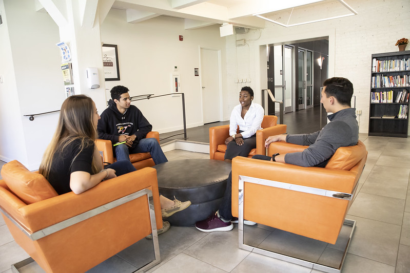 three students and a career counselor sit in lobby of career center smiling in orange chairs