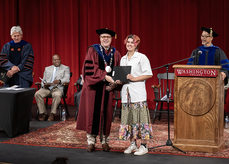 A student accepts an award from President Mike Sosulski on stage as faculty and administrators look on.