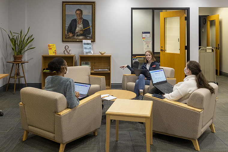 Andrea Boothby Rice talks with two colleagues as they all sit around a small table in the Miller Library.