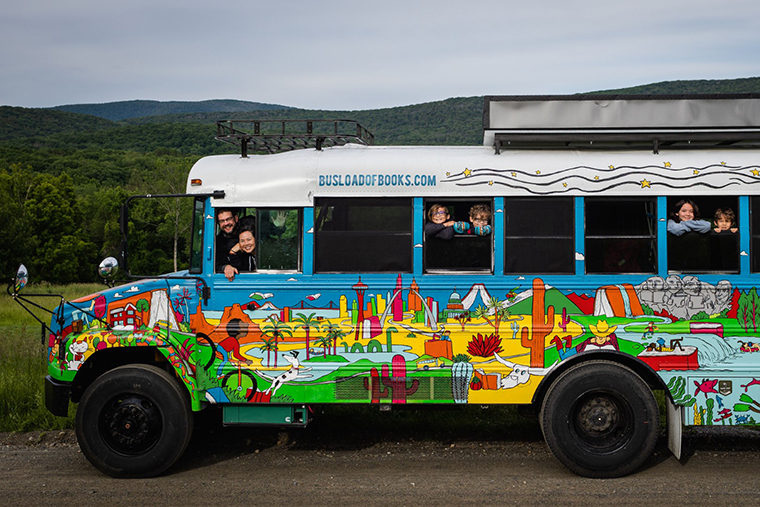 Robbi Behr and Matthew Swanson, children's book creators, and their children smile from the windows of the colorful bus they drove to schools across the country.
