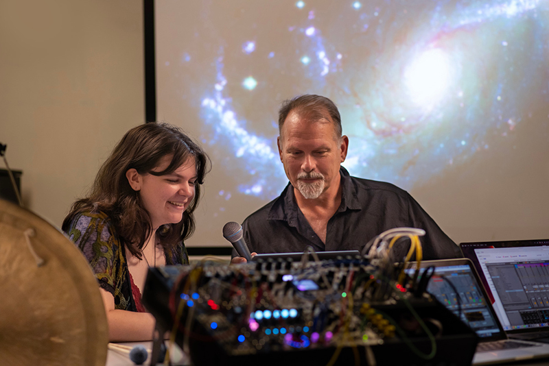 Stevie Lyles '26 and music professor Ken Schweitzer compose music to represent images from the James Webb Telescope projected behind them.