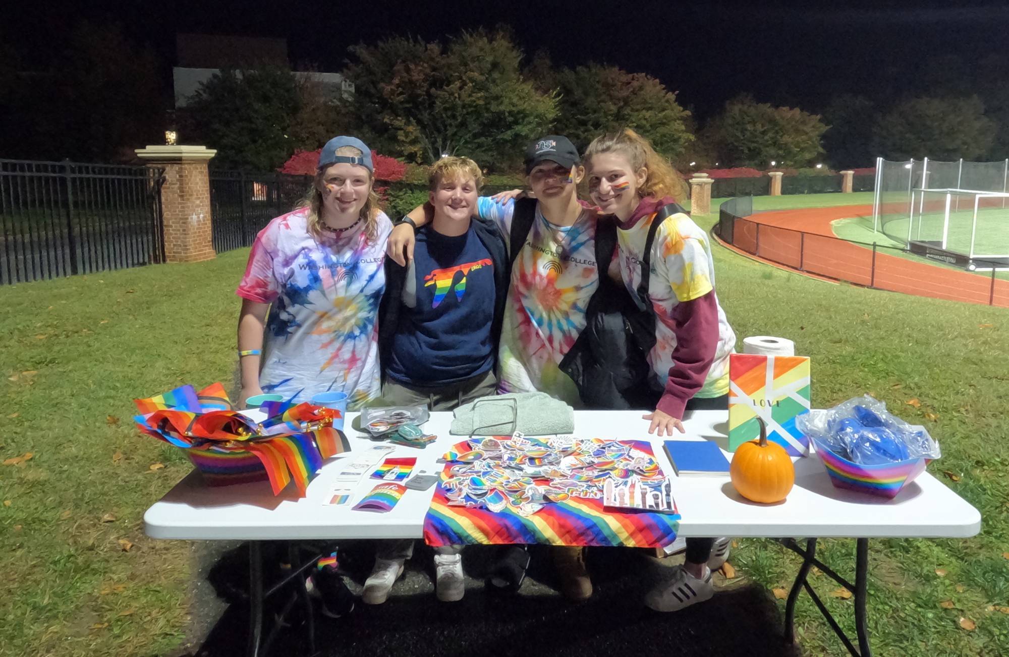 Four students at a Pride in Athletics table with materials for fans at a Washington College soccer game