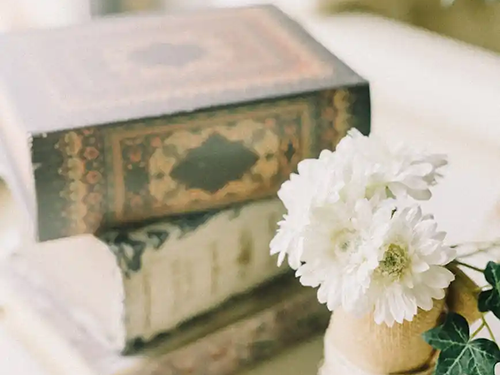 wooden vase with flowers in front of three stacked books