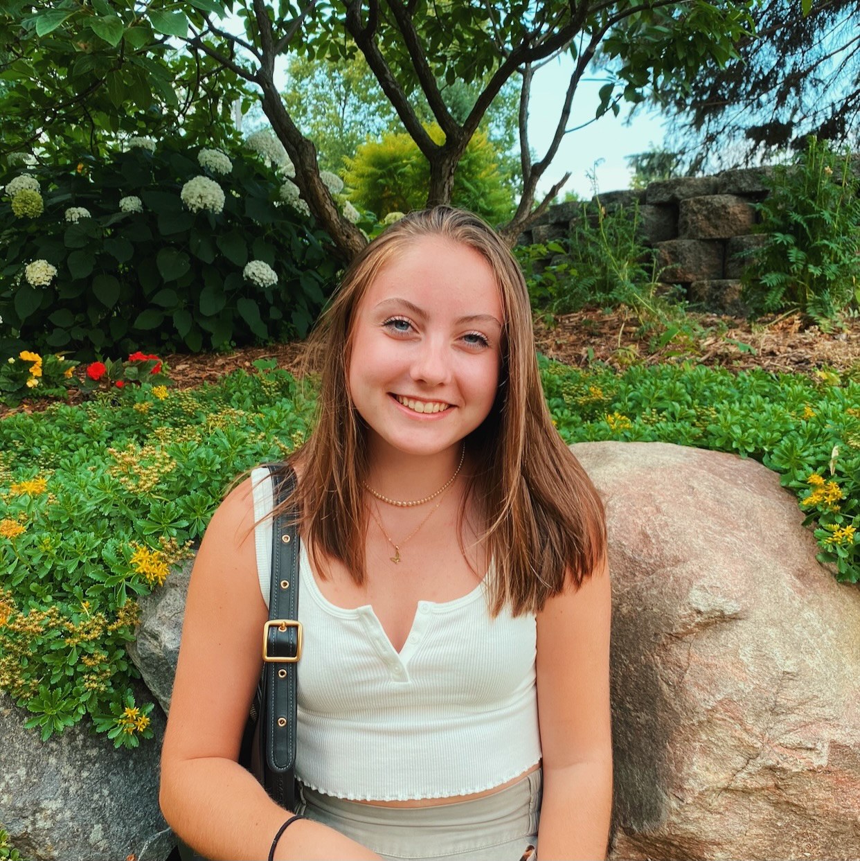 brooke outside in a blue tanktop and purse with an array of colorful flowers in the background