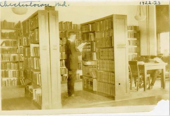 Yellowed photograph of man reading in library stacks