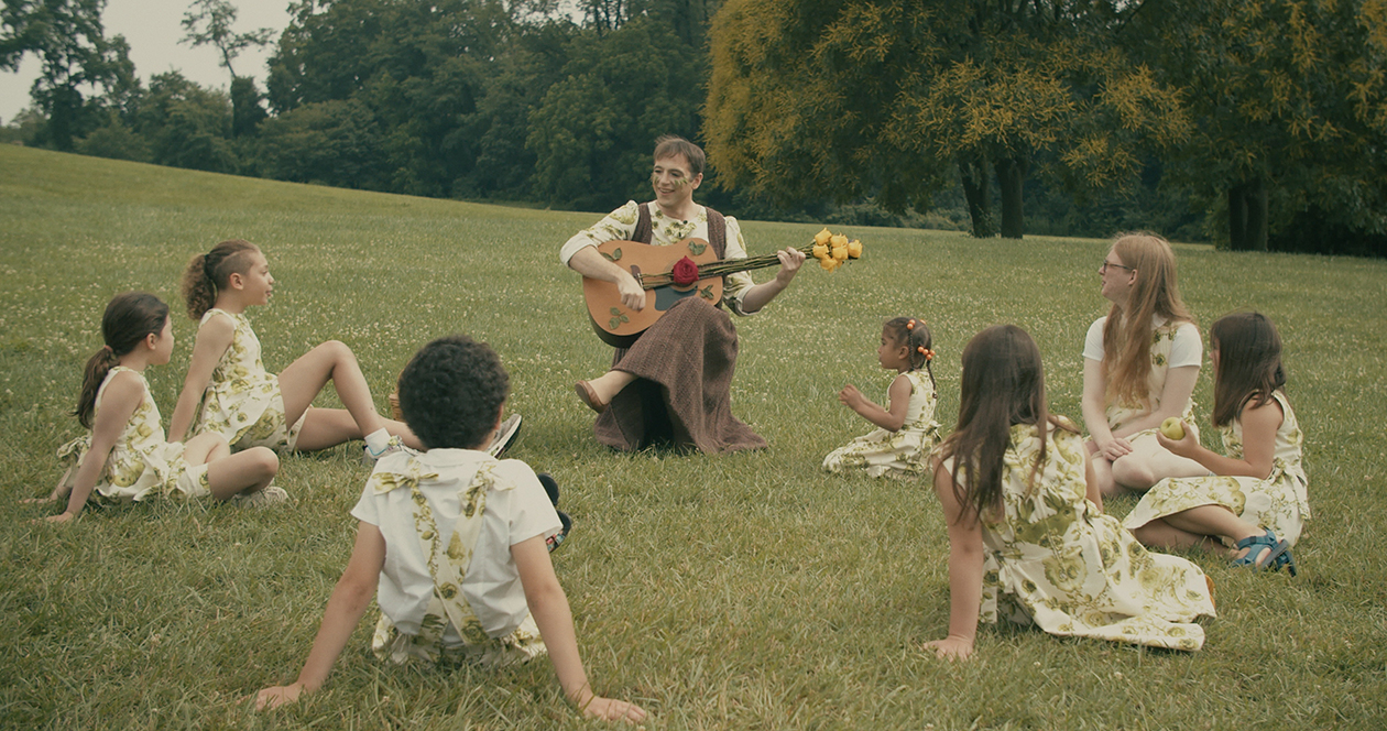 Artist John Jarboe sings to kids in a field in a still from one of her video installations