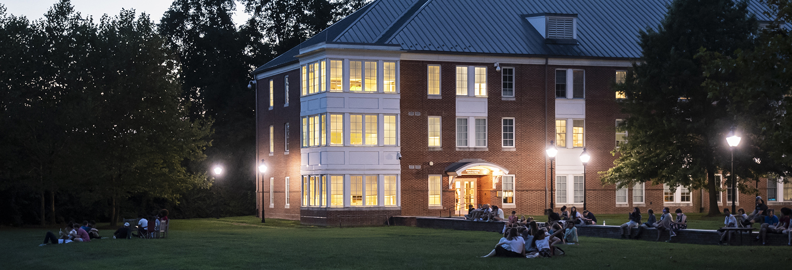 people in chairs on the lawn outside Chester Hall at nightfall