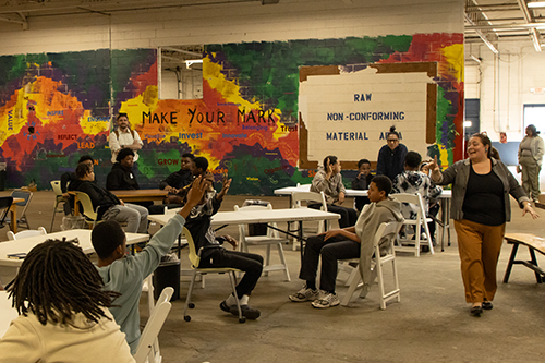 students with raised hands at tables in the Innovation Plant