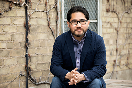 Photo of author Sequoia Nagamatsu wearing a navy blue blazer and blue checkered shirt, seated and looking ahead at the camera