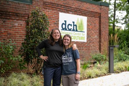 Two people stand in front of the Delaware Center for Horticulture sign on a brick wall