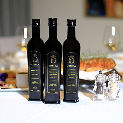Three bottles of Donika Olive Oil on a table with a meal behind