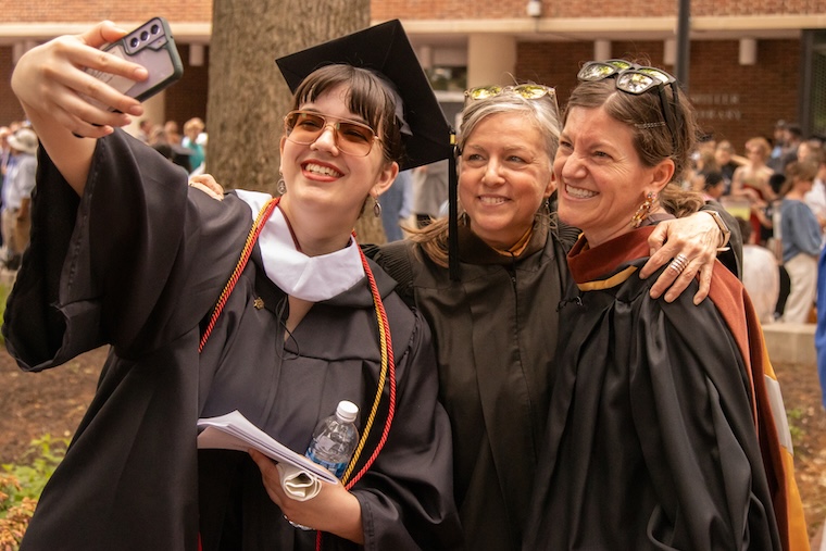 a student takes a selfie with faculty after commencement