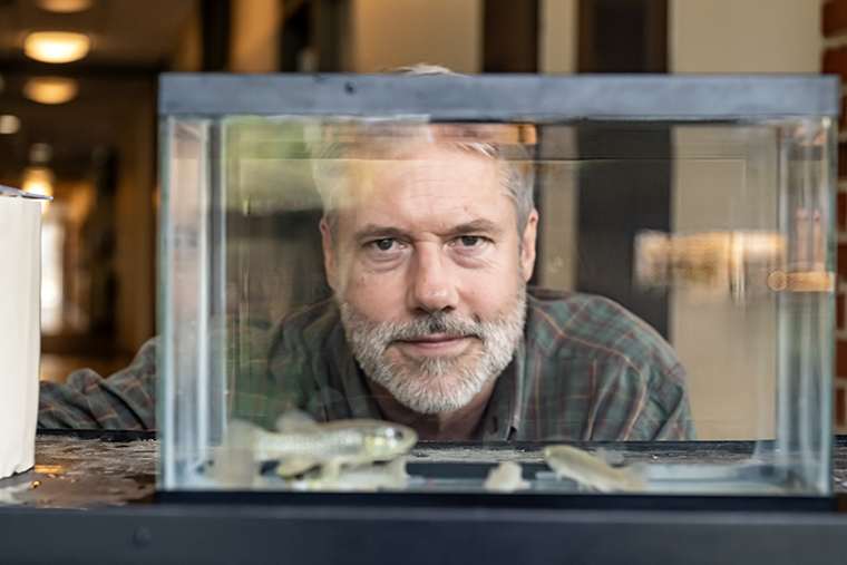 Biology professor Martin Connaughton looks at the camera through a fish tank