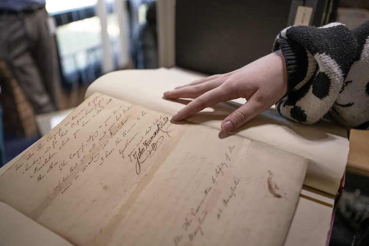 Maddie Gilliam '26 points out John Hancock's signature in an archival book in the Maryland State Archives. 