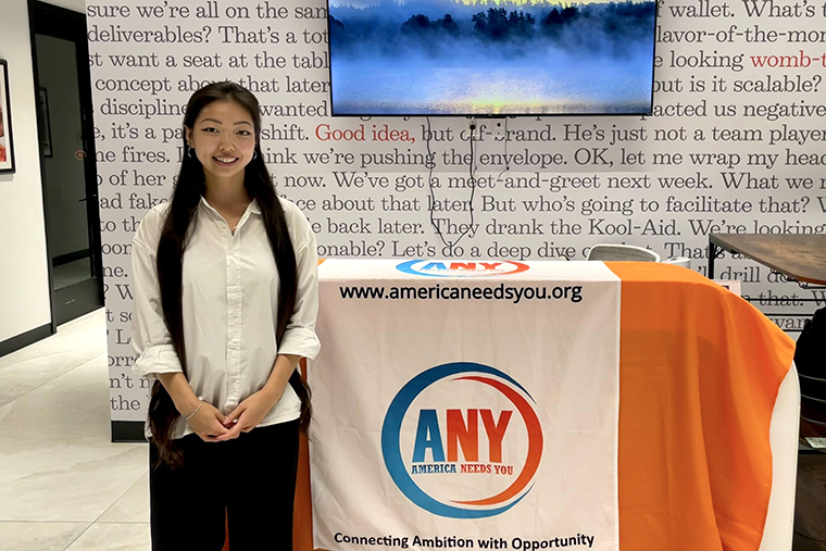 Sammy Segeda '23 stands by a booth with a sign for her current employer, America Needs You