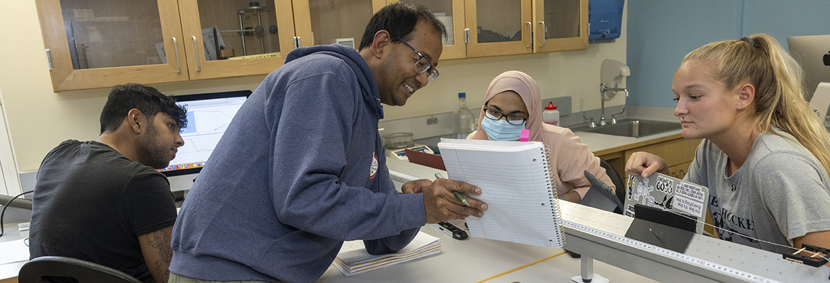 Professor Suyog Shrestha showing information in a notepad to three students in the lab