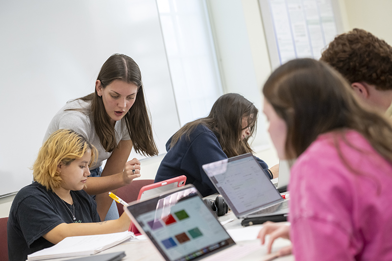 a student helps classmates looking at tablets and laptops