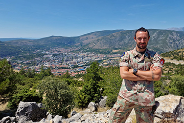 Oliver Hegglin '13 in uniform on a hilltop overlooking a town in the valley behind him