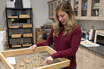 Julie Markin points to an artifact in a sifting tray she is holding in the archaeology lab