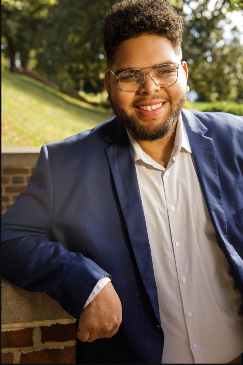 Omari, smiling and wearing glasses and a blue blazer. 